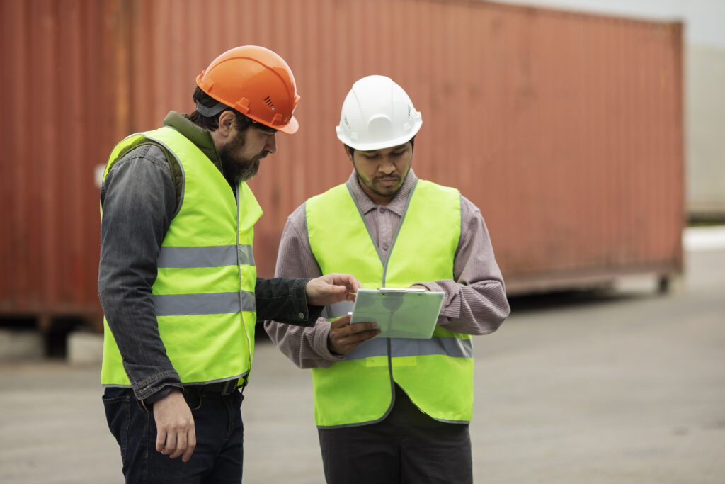 Das Bild zeigt einen externen Abfallbeauftragten, der eine weitere Person mit Schutzhelm und Warnweste über den Abfall im Unternehmen aufklärt.